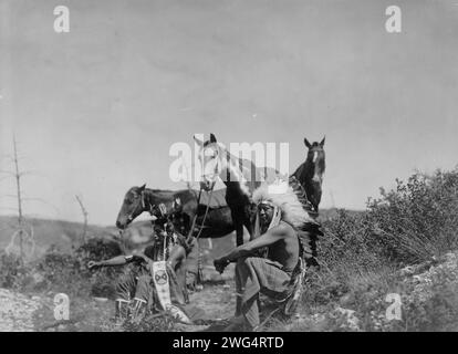 Der Vortrag, 1905. Drei Krähenmänner sitzen in felsigem Gebiet mit niedrig wachsenden Sträuchern, ihre Pferde ruhen in der Nähe. Stockfoto