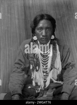 Hemd - Kalispel, 1910. Das Foto zeigt einen Kalispel-Mann, in voller Länge Porträt, nach vorne gerichtet, mit überkreuzten Beinen sitzend, Hände auf Knien. Stockfoto