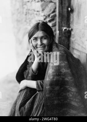 Ein Navaho-Lächeln, 1904. Das Foto zeigt eine Navaho-Frau, die vor der Tür sitzt, mit der rechten Hand auf der Wange, nach vorne gerichtet, lächelnd. Stockfoto
