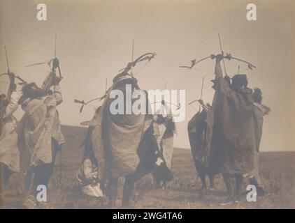 Der Flug der Pfeile, um 1908. Das Foto zeigt einen Atsina-Tanz mit Einheimischen, die sich in einem Kreis um eine zentrale Figur versammelt haben, die so posiert ist, als ob sie Pfeile in Richtung Himmel schießen würden. Stockfoto