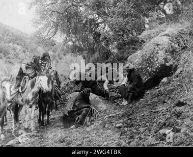 Geschichtenerzählen, 1906. Eine Gruppe von Apachen-Männern, zwei zu Pferd, andere sitzen, zuhören und zuschauen, während ein Mitglied der Partei den Boden mit einem Stock markiert. Stockfoto