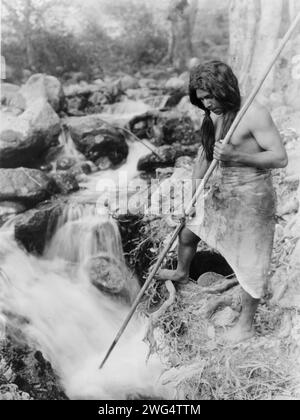 Auf der Suche nach Lachs-Hupa, 1923. Hupa-Mann mit Speer, auf der Bank stehend und in den Fluss blickend. Stockfoto