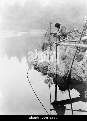 Angeln von einer Plattform aus, um 1923. Hupa Indianer auf der Plattform über dem Wasser mit einem Fischernetz. Stockfoto