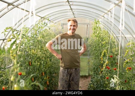 Der Bauer arbeitet in einem Gewächshaus. Ein Mann beschäftigt sich mit seinem Hobby in einem Gewächshaus und pflanzt Bio-Gemüse an. Nahporträt eines glücklichen Bauern Stockfoto