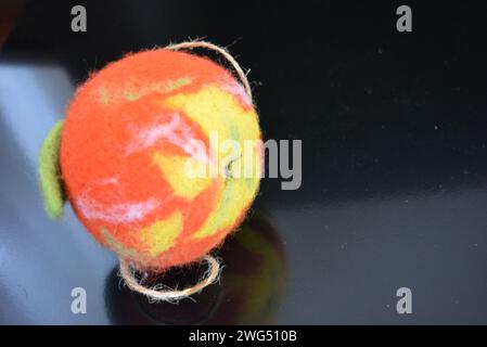 Kuscheliges ukrainisches Spielzeug aus Naturwolle und heruntergeschlagenem Filz in Form eines hellen Reifen Apfels mit fröhlichem Wurm auf schwarz matter Oberfläche. Stockfoto