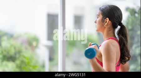 Eine junge Frau, die konzentriert und entschlossen ist, arbeitet an einer Fitnessroutine und unterstreicht ihr Engagement für das persönliche Wohlbefinden und die Fitnessziele. Hingabe an Stockfoto