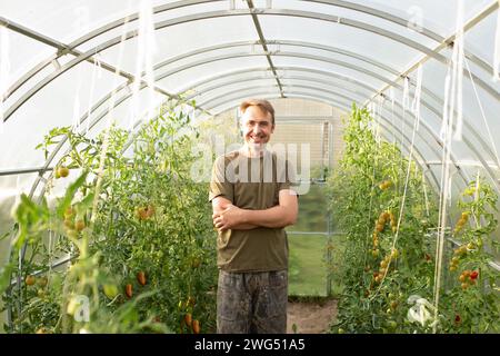 Ein Mann beschäftigt sich mit seinem Hobby in einem Gewächshaus und pflanzt Bio-Gemüse an. Nahporträt eines glücklichen Bauern im Garten und auf dem Grundstück Stockfoto