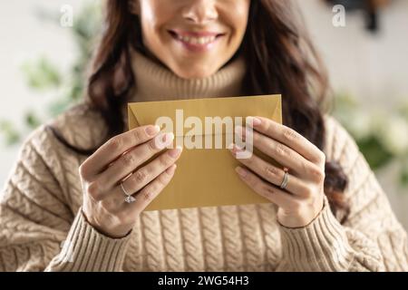 Eine lächelnde junge Frau hält einen Briefumschlag aus Recyclingpapier in den Händen. Stockfoto