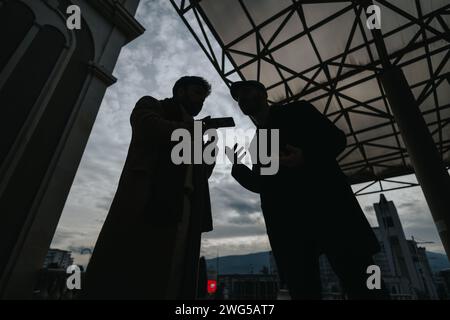 Zwei männliche Figuren mit Silhouetten führen im Freien leidenschaftliche Gespräche, wobei die bewölkte Kulisse eine dramatische Atmosphäre schafft. Stockfoto