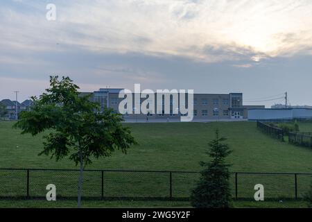 Modernes Schulgebäude - vor dem Hintergrund eines bewölkten Himmels in der Abenddämmerung - umgeben von einem gepflegten grünen Rasen - umgeben von einem schwarzen Zaun. Aufgenommen Stockfoto