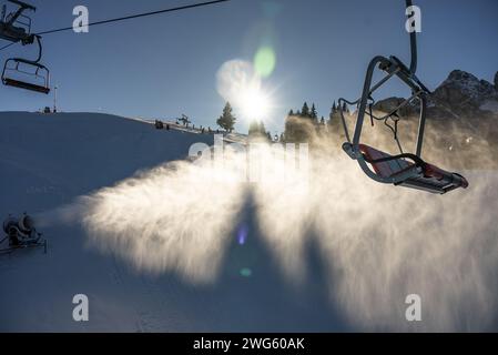 Schneekanone in den alpen, dolomiten. Schneekanonen oder Pistolen werfen Schnee auf die Skipisten. Die Sonne und die Berge im Hintergrund. Stockfoto