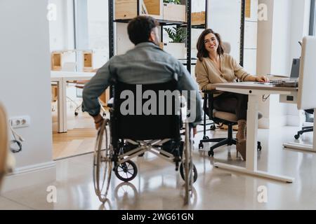Behinderter männlicher Angestellter im Rollstuhl, der seinen Rollstuhl rollte und sich seiner liebenswerten, weiblichen Kollegin anschloss. Stockfoto
