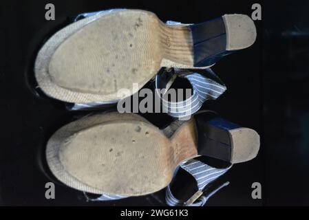 Stilvolle und ungewöhnliche Damenschuhe aus blauem echtem Lackleder und blauem Stoff. Sandalen, Sandalen, Flugschuhe befinden sich auf einem schwarzen Hochglanz. Stockfoto