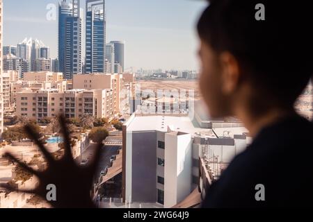 Einsamer Junge, der durch das Fenster schaut. Dubai Gebäude hinten Stockfoto