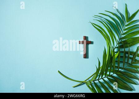 Palmensonntag. christliches Holzkreuz und Palmblätter auf blauem Hintergrund, Draufsicht, Kopierraum. Palm sunday Holiday Konzept. Stockfoto