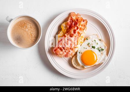 Frühstückssandwiches mit Spiegelei, Speck, Rühreier in Nahaufnahme und einer Tasse Kaffee. Spiegeleier mit Speck auf Toast und Cappuccino am Morgen. Stockfoto