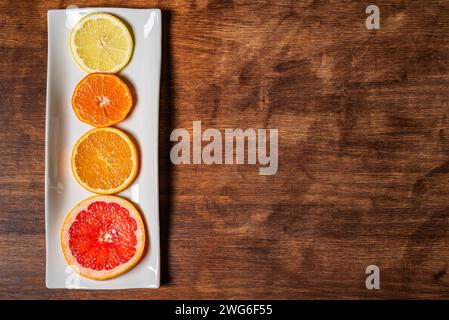 Rechteckiger weißer Teller mit Scheiben verschiedener Zitrusfrüchte, Grapefruit, Orange, Zitrone und Mandarine, auf dunklem Holztisch, mit Kopierraum. Stockfoto
