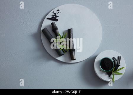 Schwarzer Bambus und eine Schüssel mit schwarzem Holzkohlepulver auf weißen Podesten mit Blick von oben. Leerraum für Werbung, abstrakte Inhalte Stockfoto