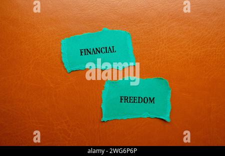 Worte der finanziellen Freiheit auf zerrissenen blauen Papierstücken mit braunem Hintergrund. Konzeptionelles Geschäftssymbol. Kopierbereich. Stockfoto