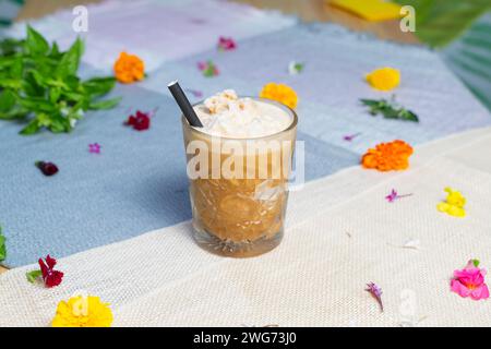 Eine Tasse Eiskaffee Latte mit Blumen im Hintergrund auf einem Tisch. Stockfoto
