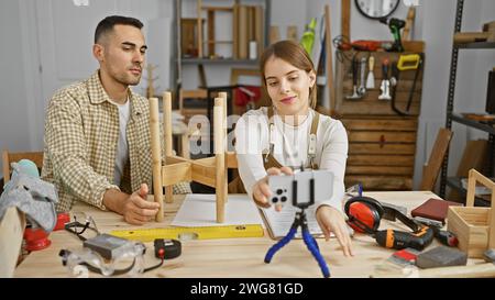 Eine Frau und ein Mann arbeiten in einer überdachten Holzwerkstatt zusammen, umgeben von Werkzeugen und Holz. Stockfoto