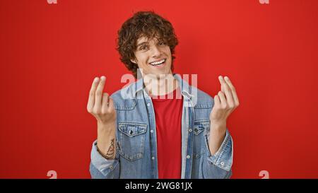 Junger hispanischer Mann mit lockigen Haaren, lächelnd und eine Geste, als würde er Geld halten, vor einem roten isolierten Hintergrund. Stockfoto