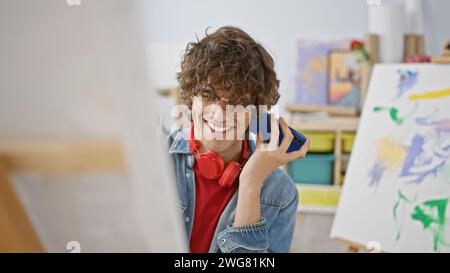 Hübscher junger Mann mit Brille und Kopfhörern, die lächeln, während sie in einem Kunststudio telefonieren. Stockfoto
