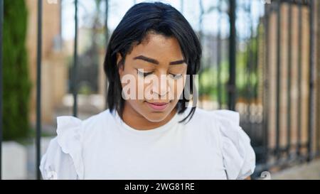 Eine besinnliche hispanische Frau in Freizeitkleidung steht draußen in der Nähe von Laub und verkörpert Schönheit und Gelassenheit. Stockfoto