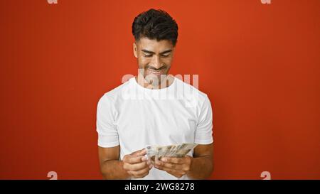 Schöner lateinischer Mann, der polnische Zloty vor isoliertem rotem Hintergrund zählt Stockfoto