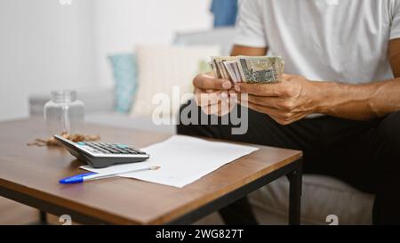 Hispanischer Mann, der zu Hause polnische Zloty-Scheine zählt, Rechner und Stift im Vordergrund Stockfoto