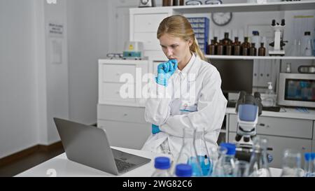 Nachdenkliche Wissenschaftlerin analysiert Daten auf Laptop im Labor Stockfoto