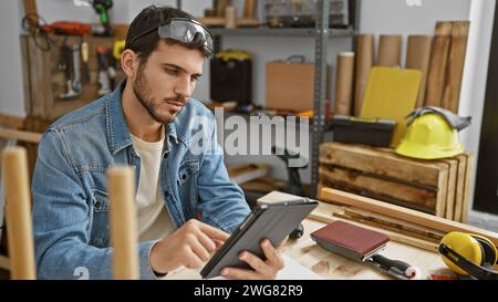 Ein hübscher junger hispanischer Mann mit Bart arbeitet an einer Tablette in einer Tischlerei. Stockfoto