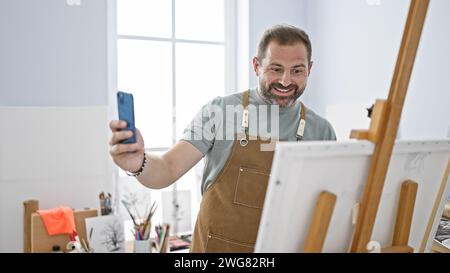 Bärtiger Mann auf Schürze, der Selfie in hellem künstlerischem Atelier macht Stockfoto