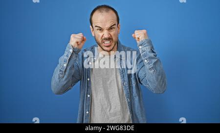 Wütender hispanischer Mann mit Bart, der draußen vor einem blauen Hintergrund posiert. Stockfoto