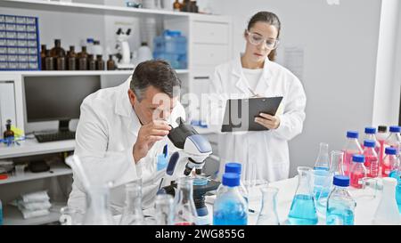 Wissenschaftler arbeiten im Labor zusammen, konzentrieren sich ernsthaft auf ihre Forschung, schreiben auf Zwischenablage, verwenden Mikroskop Stockfoto