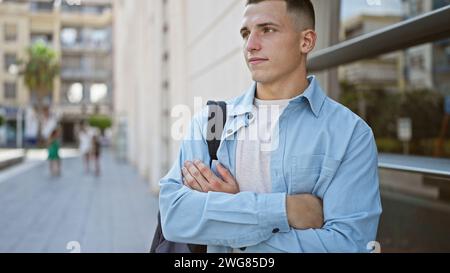 Selbstbewusster junger hispanischer Mann mit überkreuzten Armen, der auf einer belebten Stadtstraße steht. Stockfoto