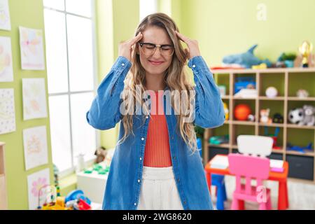 Junge Weiße, die als Lehrerin im Kindergarten arbeitet und verzweifelt und gestresst an Kopfschmerzen leidet, weil Schmerz und Migräne. Hände auf den Kopf. Stockfoto