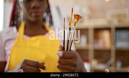 Ernsthafte aftere afroamerikanische Künstlerin, Palette und Pinsel mit Farbe, die entspannt in einem schönen Kunststudio stehen, in der Schöpfung eingetaucht Stockfoto