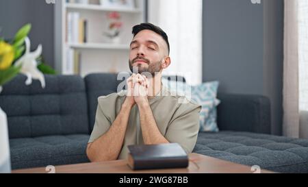 Junger hispanischer Mann sitzt auf dem Boden und betet zu Hause Stockfoto