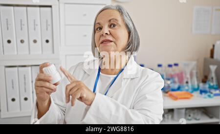 Eine reife Apothekerin untersucht Medikamente in einem weißen Labor und stellt die Professionalität des Gesundheitswesens in Innenräumen dar. Stockfoto