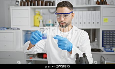 Ein bärtiger Mann im Laborkittel untersucht ein Reagenzglas in einem modernen Labor und zeigt eine professionelle Forschungsumgebung. Stockfoto
