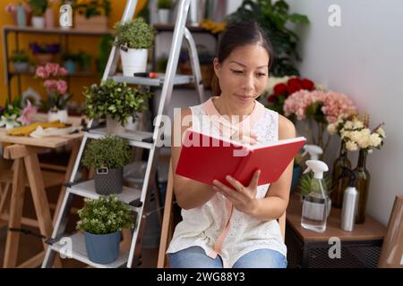 Eine junge asiatische Floristin lächelt selbstbewusst auf Notizbuch im Blumenladen Stockfoto