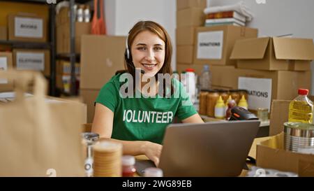 Eine junge Frau meldet sich freiwillig mit Laptop und Kopfhörern und lächelt im Wohltätigkeitszentrum Stockfoto