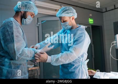 Porträt eines Arztes, der dem Chirurgen hilft, sterile medizinische Handschuhe anzuziehen. Ärztinnen und Ärzte, die sich im Operationssaal der medizinischen Klinik für die Operation vorbereiten Stockfoto