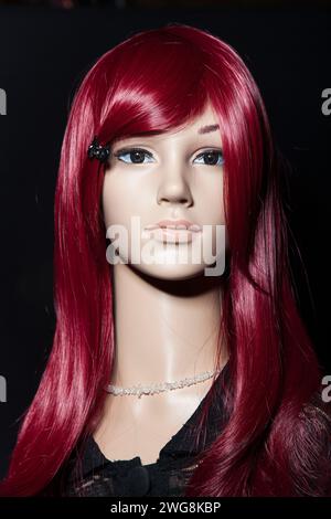 Plastikpuppe mit langen roten Haaren, die auf schwarzem Hintergrund posiert Stockfoto