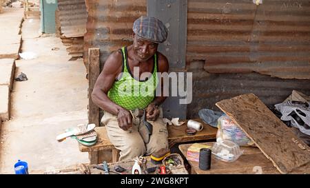 Schuhmacher-Schuster Nima Accra Ghana Afrika Armut. Der alte muslimische Schuhmacher und Schuster. Armutsabteilung von Accra Ghana. Primitive Werkzeuge im Außenbereich. Stockfoto