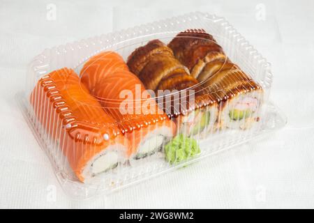 Ein appetitliches Sushi-Set mit Lachsnigiri und Aalbrötchen, das in einer durchsichtigen Plastikkiste zum Mitnehmen angeordnet ist, komplett mit grünem Wasabi. Stockfoto