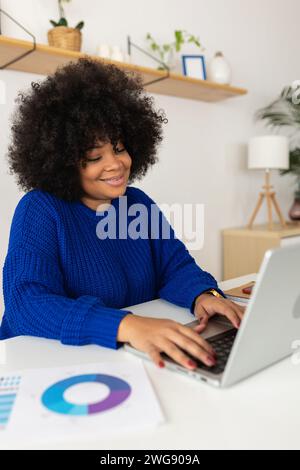 Lächelnde junge lateinamerikanische Frau, die zu Hause am Laptop arbeitet Stockfoto