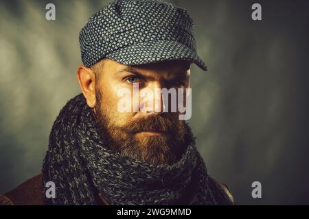 Nahaufnahme eines bärtigen Mannes in Lederjacke, Wollschal und Mütze. Legere Winterkleidung. Hübscher, stylischer Mann in Strickschal gewickelt Stockfoto