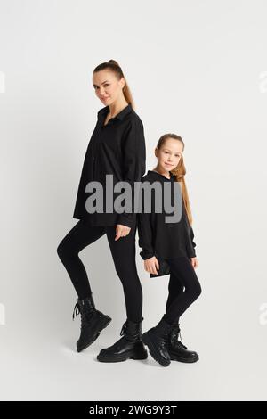 Mutter und Tochter in ähnlichen schwarzen Outfits stehen hinten an hinten Stockfoto